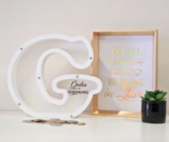 Personalizuota taupyklė raidės „G“ formos su vardiniu užrašu ir dekoratyvine aplinka.