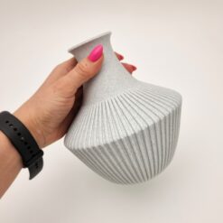 Rifliuota vaza sausoms gėlėms laikoma rankoje, matomas jos dydis ir forma.